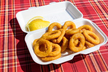 Large group of freshly fried calamari and onion rings on display for sale at a street food festival, ready to eat healthy seafood, beautiful orange monochrome outdoor background