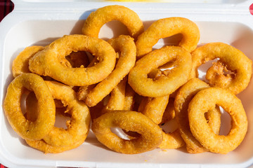Large group of freshly fried calamari and onion rings on display for sale at a street food festival, ready to eat healthy seafood, beautiful orange monochrome outdoor background