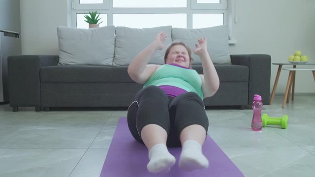 Plus size female working out hard at home, doing abs exercise to lose belly fat