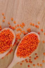 Flat lay. Two wooden spoons with orange lentils on the table. Wooden spoons close up at the bottom of the frame. Top view on lentil grains. Close-up, vertical, top view, free space at the top.