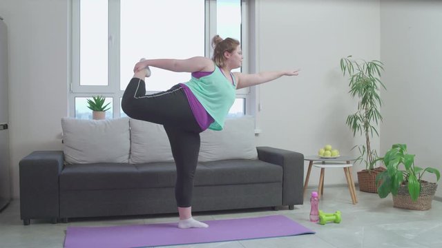 Clumsy plus size girl doing yoga exercise home, working out to be fit and slim