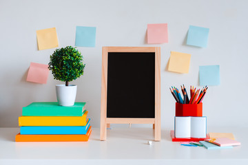 Student creative desktop layout with colorful stationery, colored pencils and bright books on a white wall background.
