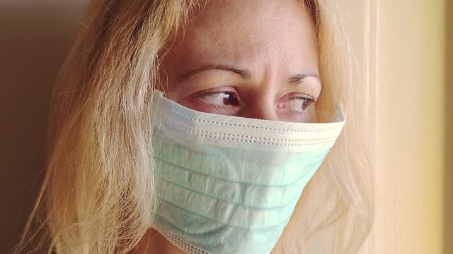 SLOW MOTION: blonde woman with a sanitary mask and shining eyes looking outside. Concept of outbreak, quarantine for the corona-virus.