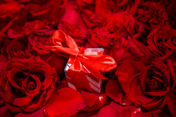 A gift box with a red bow lies in red roses.