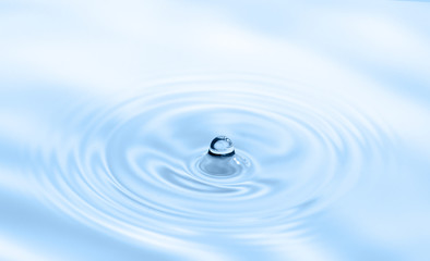 Naklejka na ściany i meble Water drop falling into water making splash and ripples. Light blue nature background.