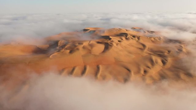 Aerial view from a drone rotating around a massive sand dune that is overcome by thick fog clouds. Liwa desert, Abu Dhabi, United Arab Emirates.
