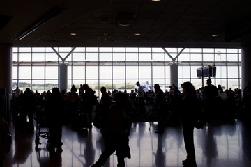 A large group of people in silhouette, waiting in the airport terminal to board the plane.	