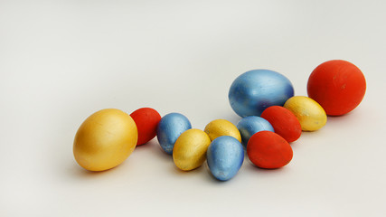 yellow gold red blue and blue large and small multicolored Easter eggs lie on a white background for Easter
