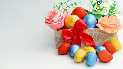 Easter eggs of large sizes and bright colors are in a beautiful box with flowers and small colored eggs are freely lying near the box