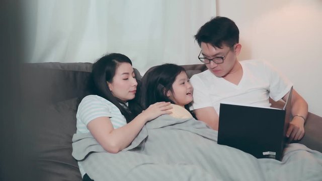 young attractive asian mom reading Children's stories to pretty cute daughter child on sofa in living room night time leisure activity