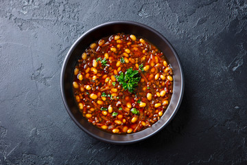 Bean soup in a black bowl. Dark background. Close up. Top view.
