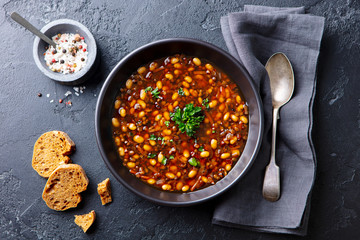 Bean soup in a black bowl. Dark background. Top view.