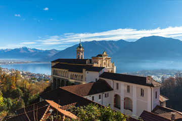Stunning panorama view of Madonna del Sasso church above Locarno city with Lake Maggiore, snow covered Swiss Alps mountain and blue sky cloud in background on autumn sunny day, Ticino, Switzerland