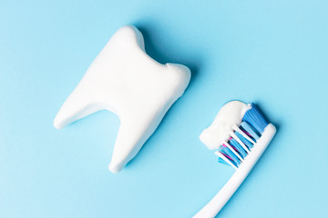 Toothbrush with toothpaste and white tooth on blue background, concept of healthy oral cavity.