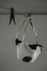 A white medical mask with green air filter hanging on a clothesline.