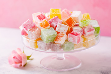 Assorted Turkish delights on glass cake stand. Pink background. Close up.