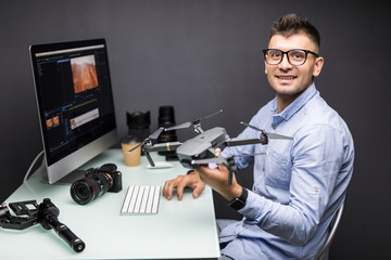 Fototapeta na wymiar Young man sitting at table with different devices and gadgets holding drone in hands in office. Young creative designer thoughtful look away in private office