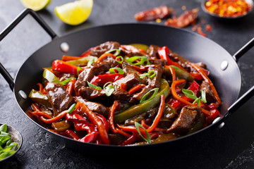 Beef and vegetables stir fry in a pan. Dark background. Close up.