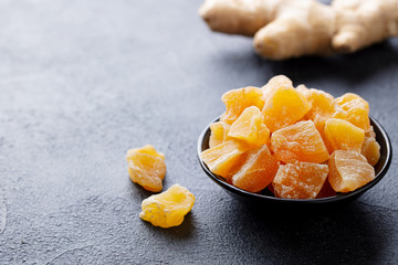 Candied ginger in black bowl on dark stone background. Close up. Copy space.