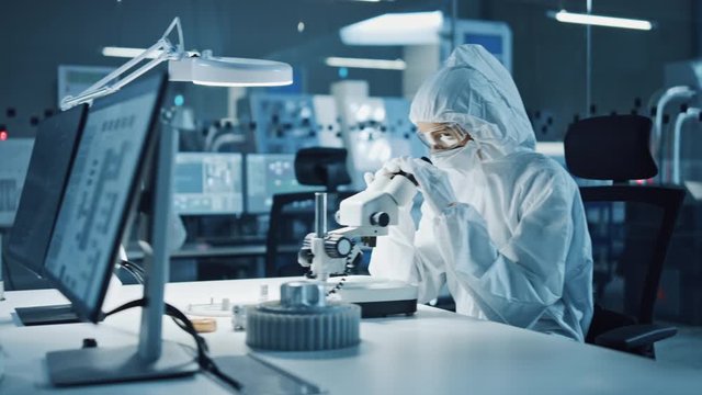 Modern Factory: Team of Engineers and Scientists in Clean Sterile Coveralls Work on Desktop Computers, Use Microscope, Developing Electronics for High-Tech Medical Electronics Research