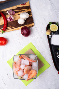 frozen shrimps  in bowl with vegetables on white table. flat lay