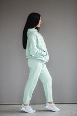 Attractive young model in tracksuit. Woman demonstrating clothes in studio. Gray background