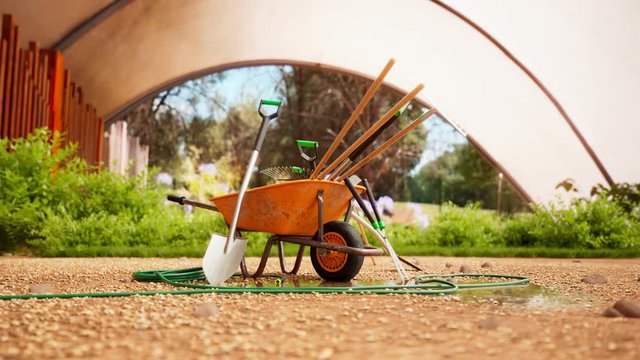 Garden tools gathered around a wheelbarrow in a beautiful, lush garden. 4KHD