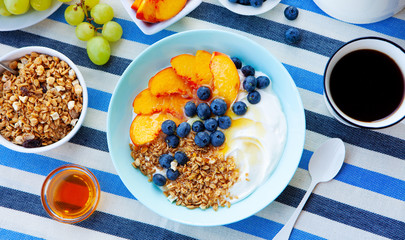 Healthy breakfast, muesli, granola with yogurt, fruits and berries in blue bowl. Stripped textile background. Top view.