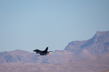 F-16 Fighting Falcon against the Nevada hills, with missiles on the wing and  
the jet stream visible behind the aircraft
 - obrazy, fototapety, plakaty