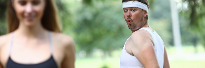 Portrait of surprised man looking at sexy sportswoman with interest. Pretty woman running and doing physical exercises in park. Sport and fitness concept