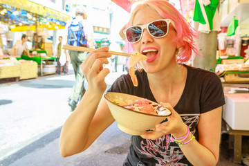 Caucasian lifestyle tourist woman eats with chopsticks, sashimi salad at Ameya-Yokocho market...