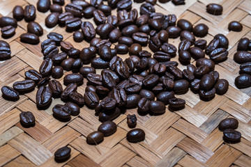 Roasted coffee beans scattered on traditional woven bamboo mat. Dark food background concept.