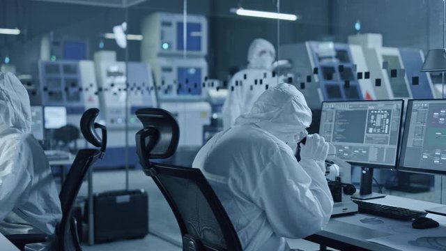 Research Factory Cleanroom: Team of Engineers and Scientists in Coveralls Work on Computers, Use Microscope to Inspect Motherboard Microprocessor, Developing Electronics for Medical Electronics