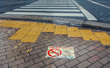 Small No smoking sign on pavement next to pedestrian crossing in Tokyo, Japan
