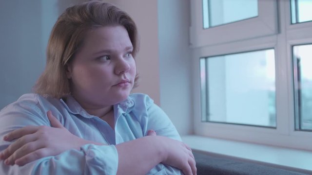 Sad plump girl looking in window, feeling depressed and lonely, insecurities