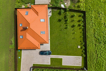 Aerial top view of house shingle roof with attic windows and black car on paved yard with green...