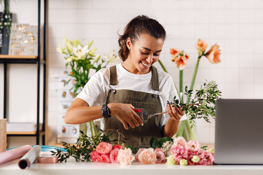 Smiling woman working at counter. Female florist cutting flowers with scissors.