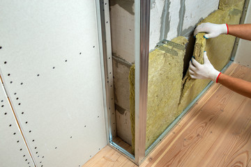 Worker insulating a room wall with mineral rock wool thermal insulation.