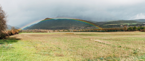 Obraz premium View of a rainbow coming out, in a valley with the mountains in the background.