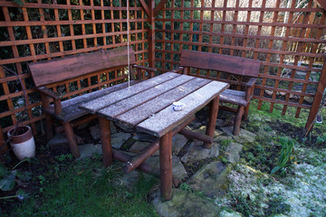 wooden furniture sprinkled with snow in the gazebo