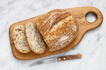 Round loaf of freshly baked sourdough bread with knife on cutting board, top view. Artisan bread...