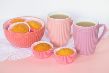 pink porcelain tea cups and muffins in a pink bowl and on the table close-up on a pink background. background with tea cups and muffins.