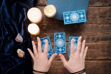 Fortune teller with tarot cards in the hand on brown table background.