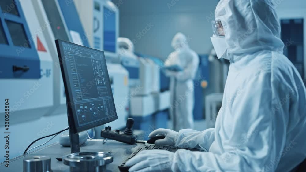 Aufkleber factory cleanroom: engineer wearing coverall and mask does system control on a computer, uses contro