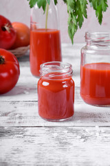 Tomato juice in glass jars on white wooden table