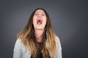 Dreamy  female with pleasant expression, wearing casual clothes, looks sideways, keeps hand under chin, thinks about something pleasant, poses against gray background.