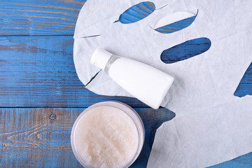 Cloth cosmetic face mask, cream and scrub on blue wooden table