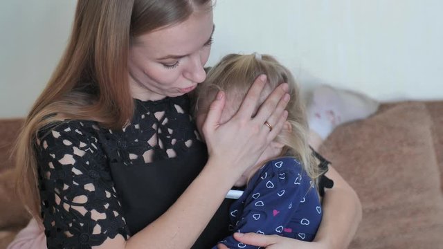 Caring mother in a bandage measures her daughter's temperature.