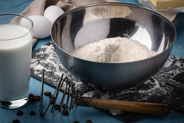 Flour in a steel bowl, a glass of milk and eggs