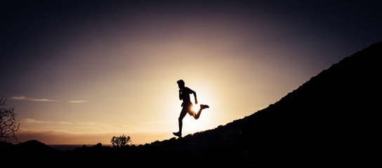 one man running and doing jogging alone in the mountains with the sunset at the background - active people and healthy and fit lifestyle concept